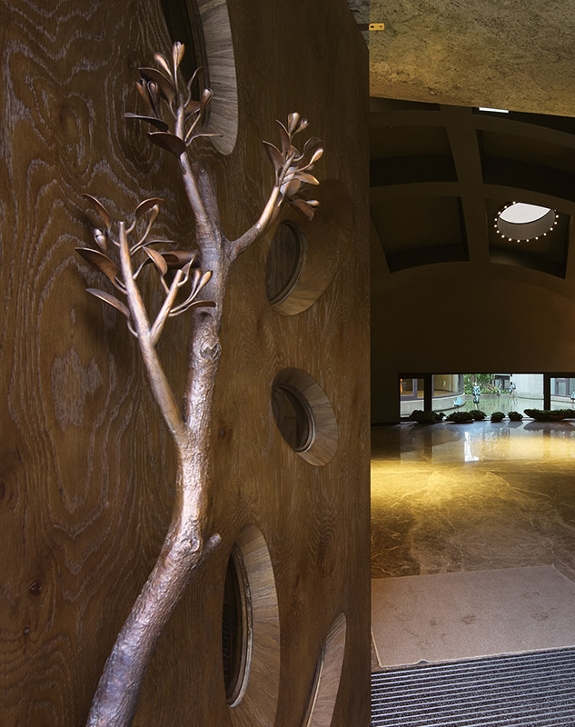 The community's wooden door resembles the trunk of a grand tree, with handle extending like branches and window openings fanning out like leaves. The handle position and window heights are ergonomically designed, ensuring that each time the door opens, it resonates with the creator's artistry. – Sunny Happiness Gendii